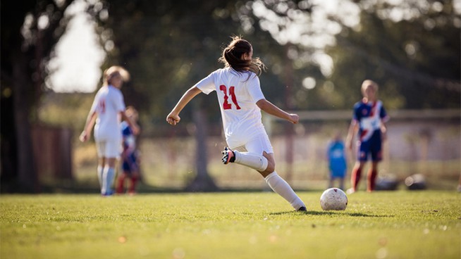 Back view of female soccer player kicking the ball during a match on a stadium.