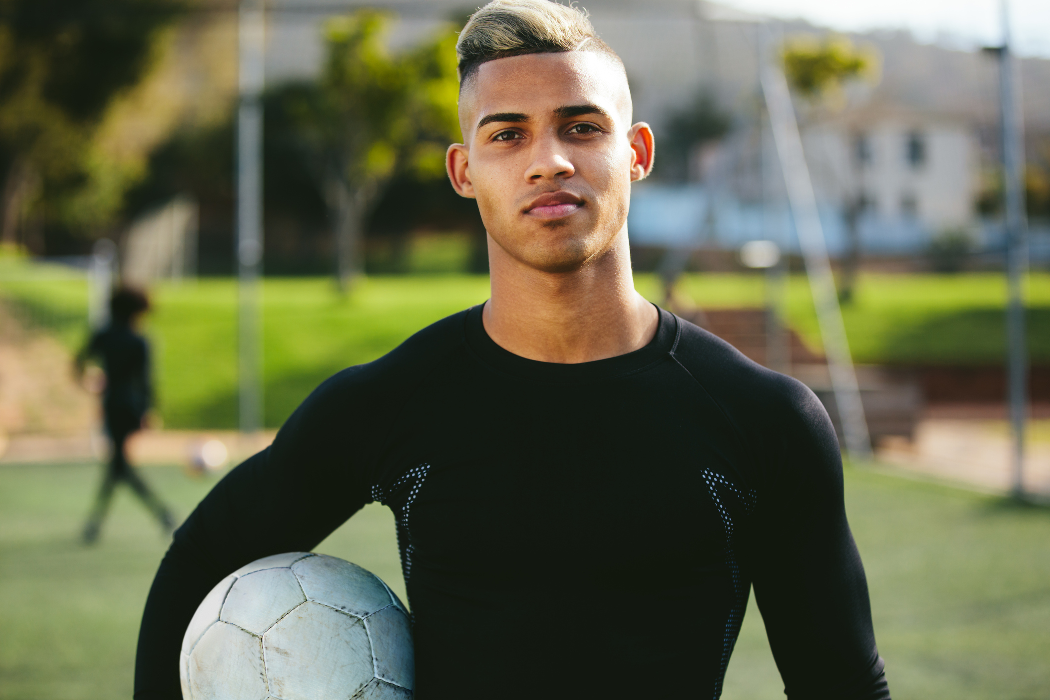 Portrait of teenage soccer player holding a football in his hand and looking at camera. Young man during training on football field.