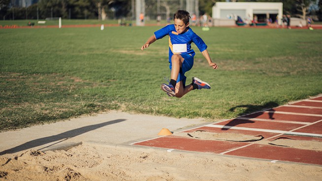 Little boy is in mid-air as he does a long jump at athletic club.