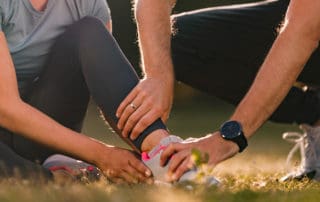 Close up of unrecognizable man assisting his wife with ankle pain during sports training in nature. Copy space.