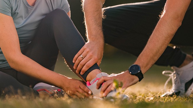 Close up of unrecognizable man assisting his wife with ankle pain during sports training in nature. Copy space.