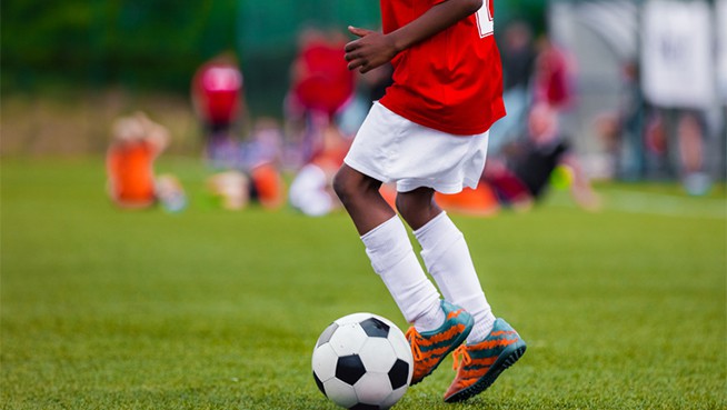African American Boy in Junior Football Team Leading Ball on Grass Training Field. Youth Soccer Player Kicking Ball
