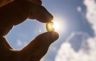 image of hand holding a small vitamin d tablet in front of the sun outside.