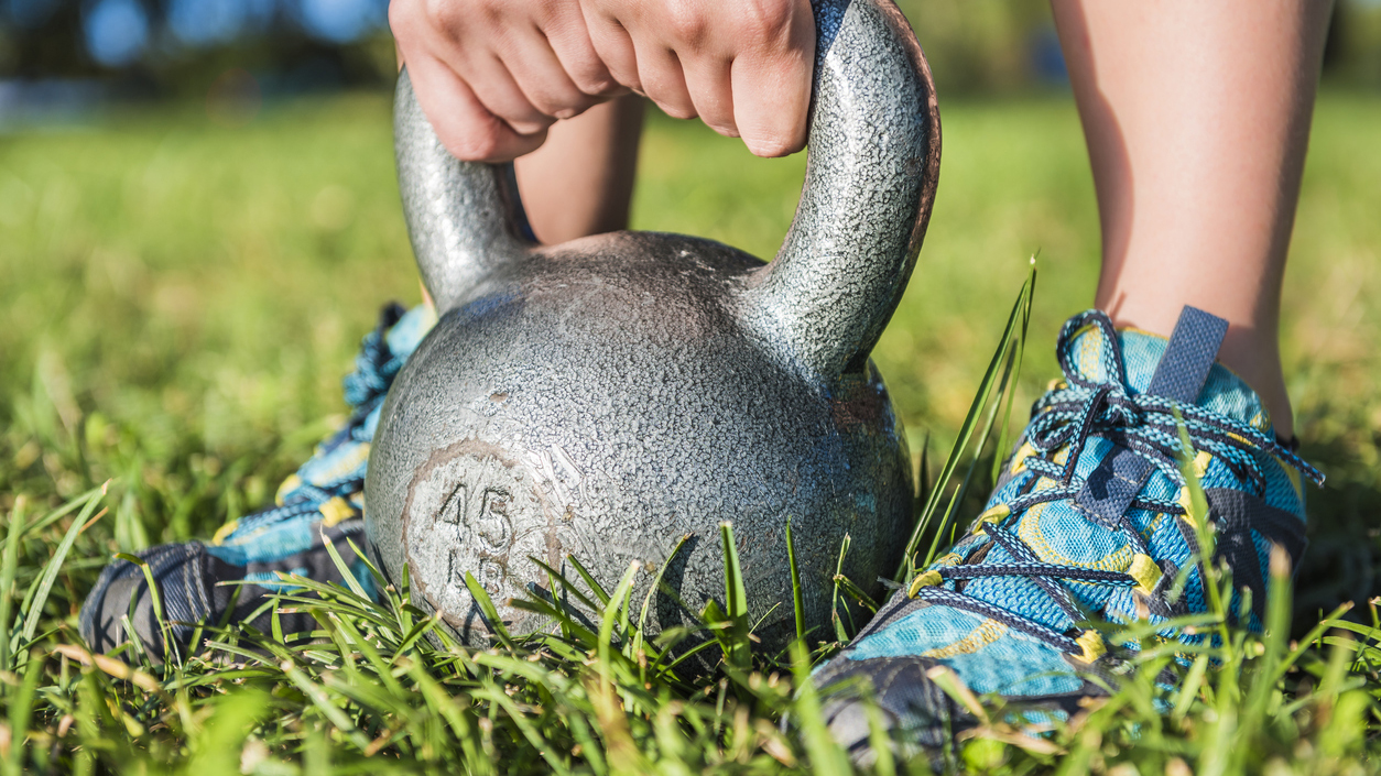 Closeup of woman's legs with sneakers in grass and hands picking up 45 pound kettlebell