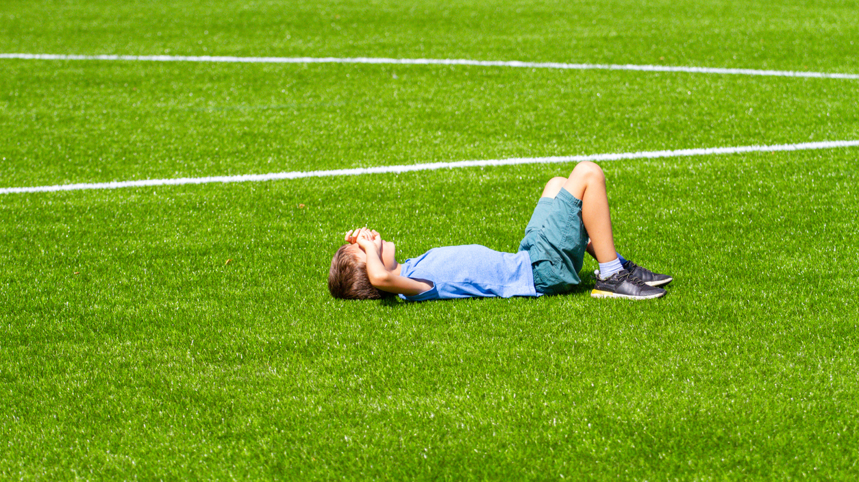 Boy lying on green football soccer field