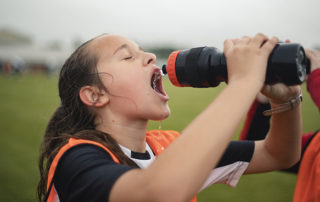 Close-up of a teenage girl squirting water into her mouth from her water bottle during a break at her football practice.