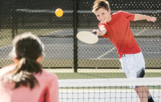 Two young people playing the game of pickleball on a court.