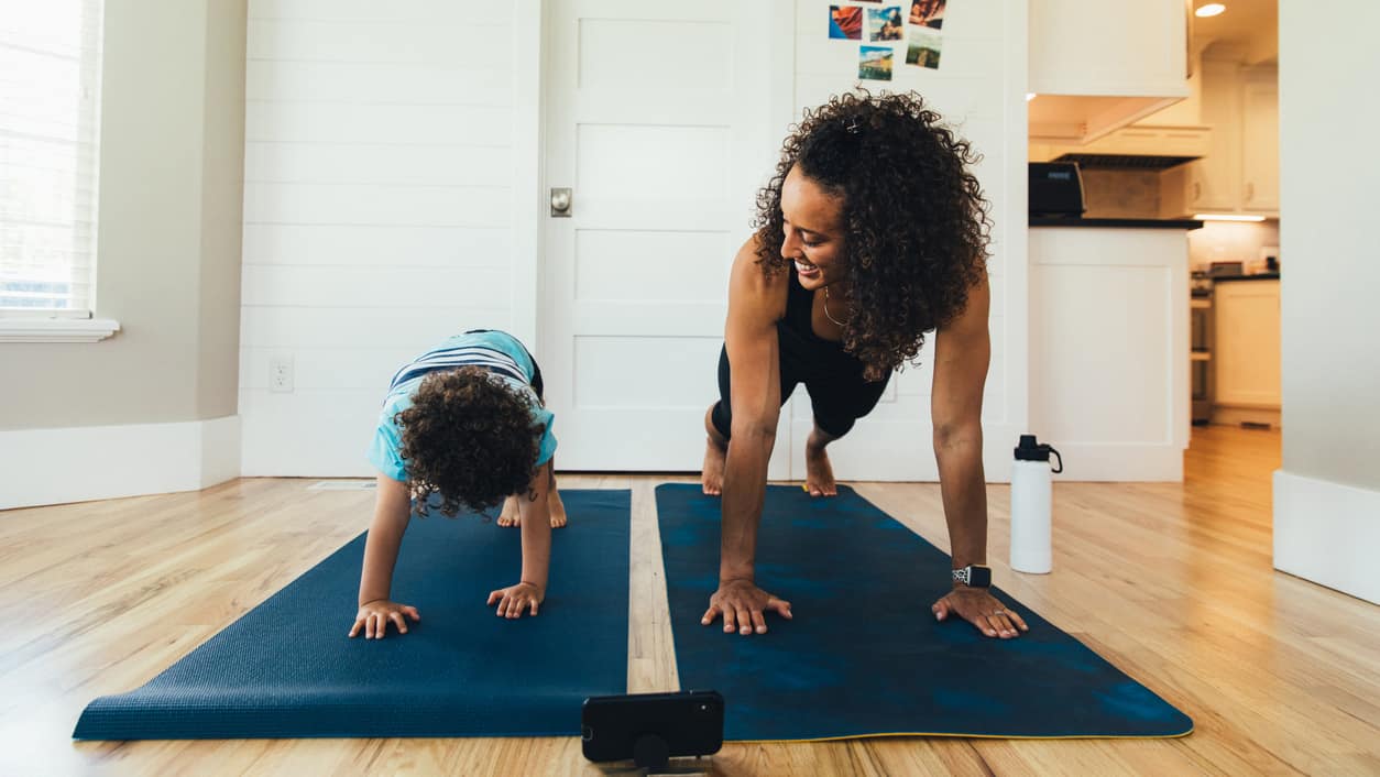 A mother exercises with her young son inside their home. She is teaching the boy the importance of a healthy lifestyle by proper stretching and exercising.