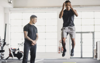 Young man having a personal training session in the gym. He is doing warm up exercises while his personal trainer guides him.