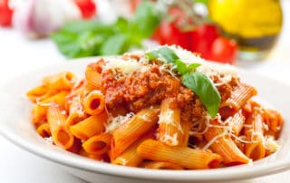 Plate of penne bolognese with ingredients in the background.