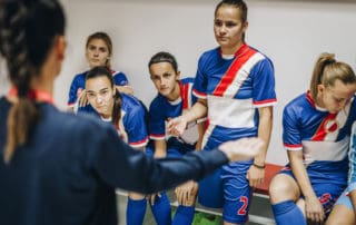 Girls soccer coach having talk with girls soccer team in locker room