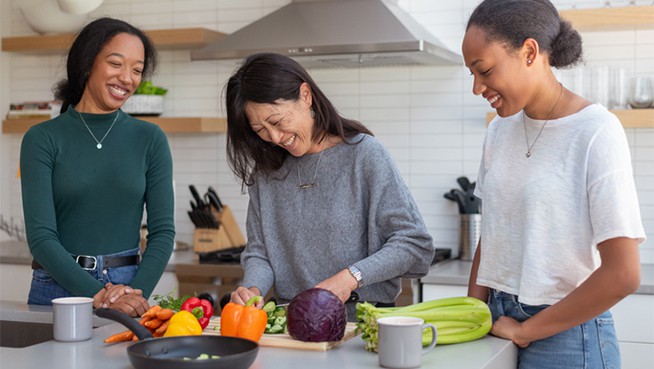 An woman of Asian descent cooks a healthy meal in a modern kitchen with the help of her two mixed race teenage daughters
