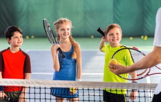 Excited children are listening to explanations of their tennis trainer with attention. They are holding rackets and laughing. Portrait